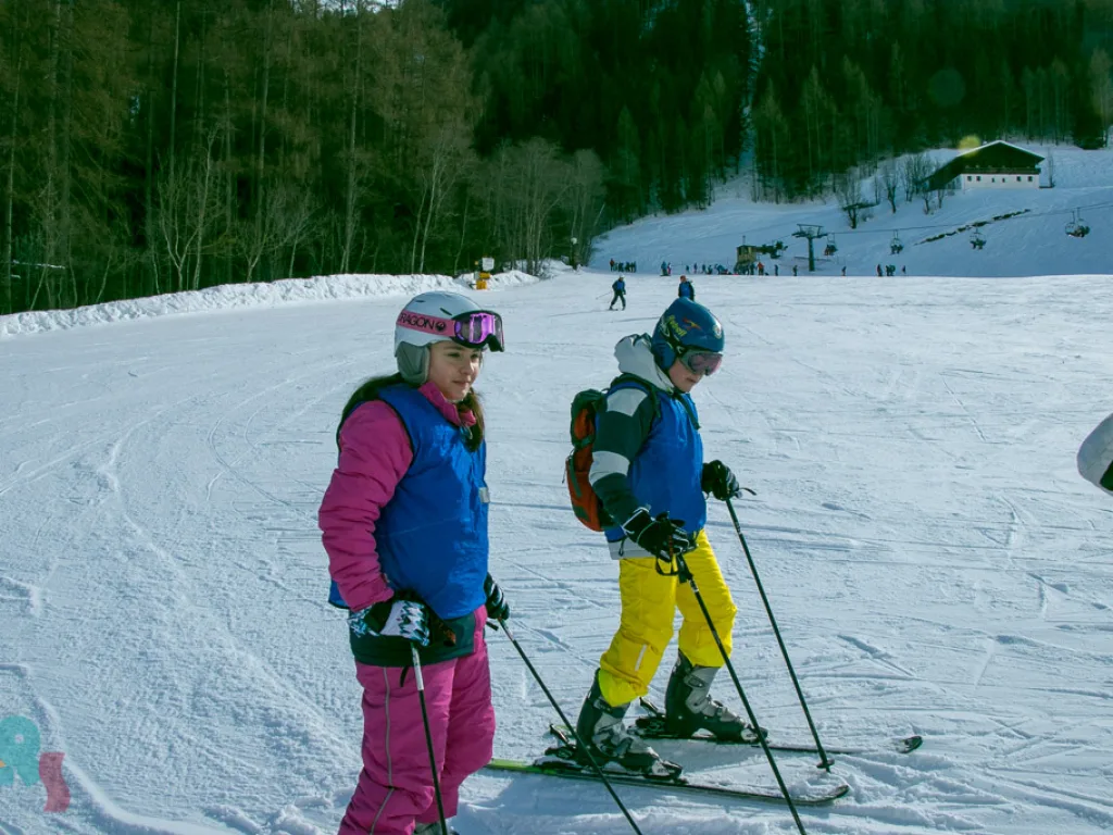 Zwei Skifahrende auf der Piste am Waldrand.